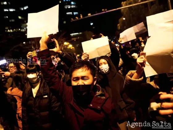 Cientos de chinos se reúnen para una vigilia y sostiene hojas de papel blanco en protesta por las restricciones contra el coronavirus, mientras conmemoran a las víctimas de un incendio en Urumqi (REUTERS/Thomas Peter)